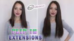 Ženska z lasmi do ramen na levi in dolgimi, voluminoznimi lasmi na desni. Na obeh slikah nosi sivo srajco in se smehlja. Besedilo se glasi "Flip In Extensions" na dnu in "Oxy Extensions" zgoraj na sredini.
